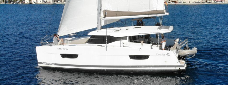 Der Katamaran Lucia 40 „Leon" unter Segeln vor einem Küstenort bei Rogoznica – Yachtcharter Kroatien